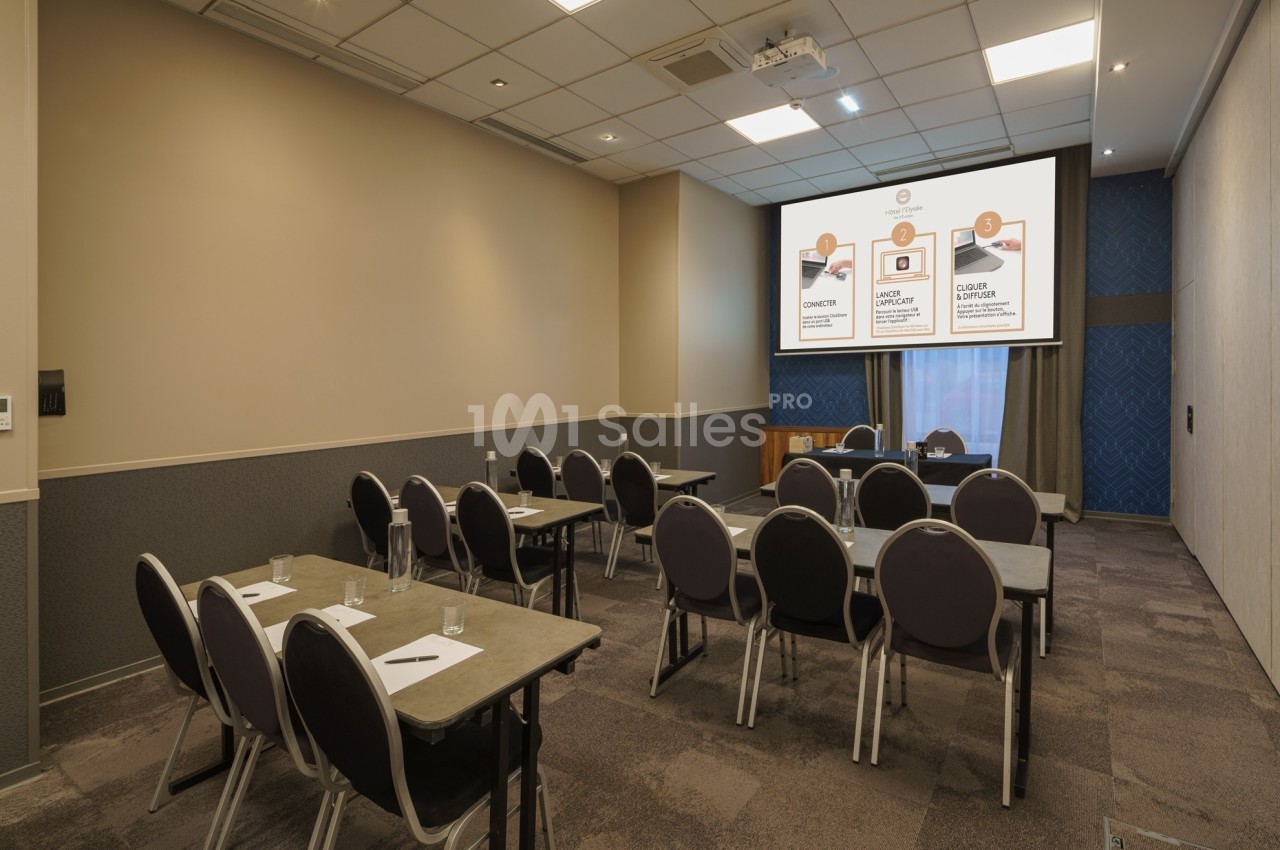 Salle de conférence avec des tables, chaises alignées et un écran de présentation affichant des graphiques.