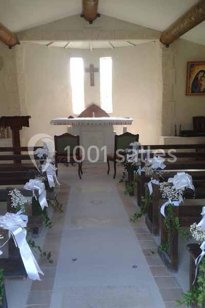 Intérieur d'une petite chapelle décorée pour un mariage, avec bancs ornés de rubans blancs et fleurs.