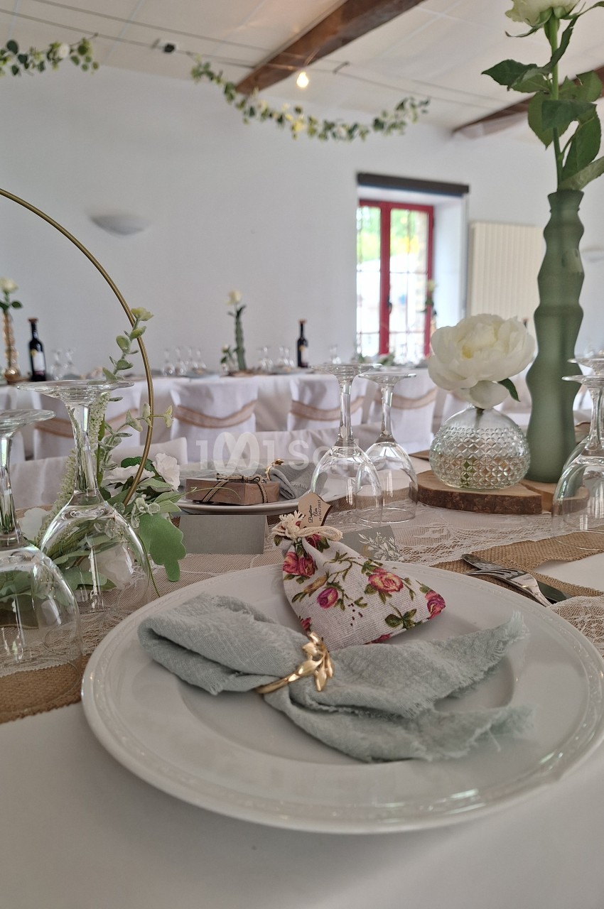 Table décorée pour un mariage avec assiette, serviette pliée, rond de serviette doré et détails floraux élégants.