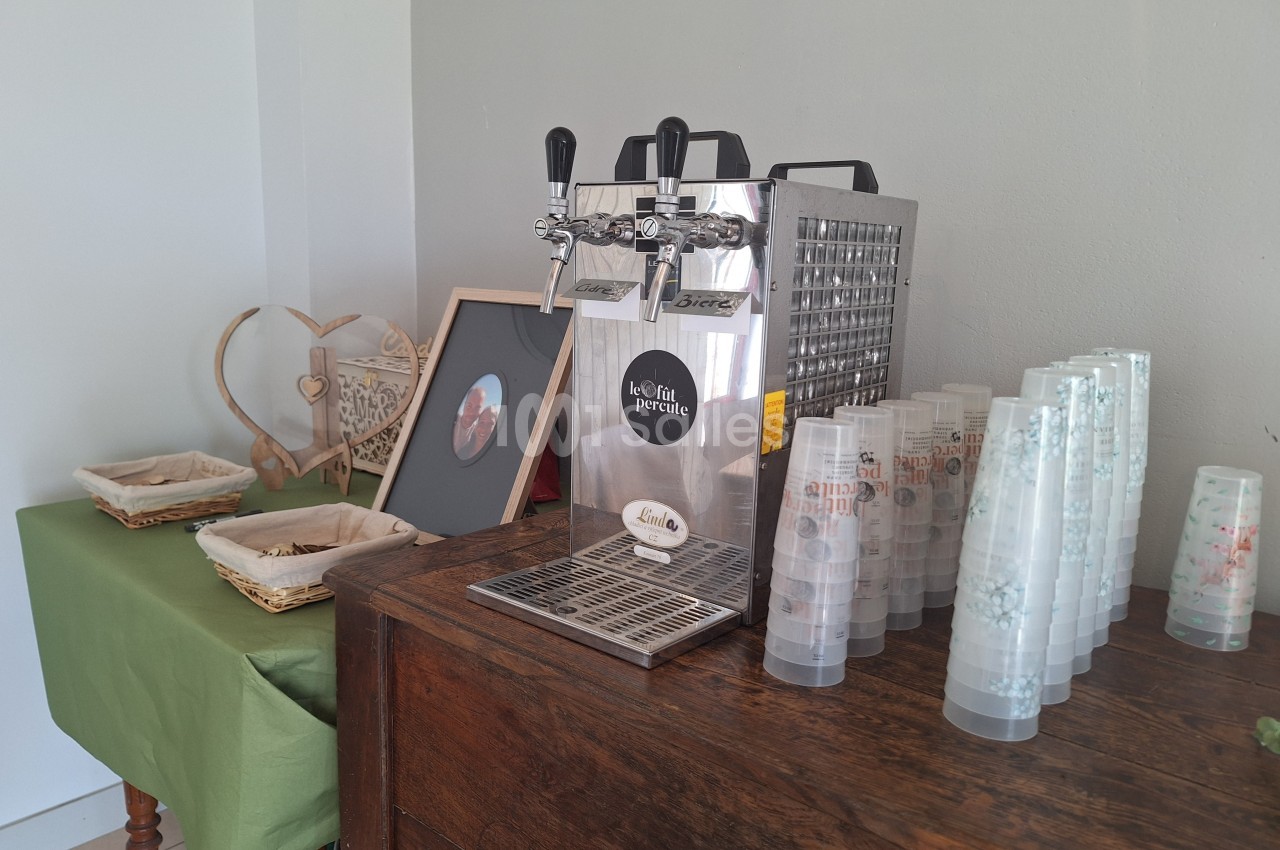 Distributeur de boissons avec gobelets en plastique empilés sur un meuble en bois, décoré d'éléments rustiques.