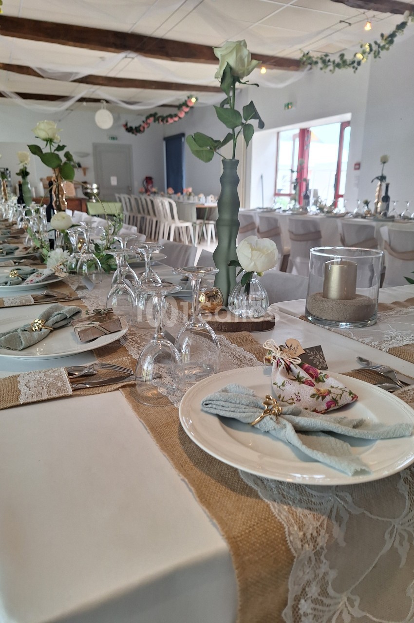Table décorée pour un événement, avec nappes en toile de jute et dentelle, vaisselle élégante et fleurs blanches.