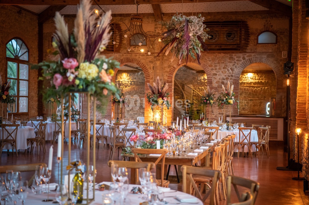 Salle de réception décorée avec des tables dressées, des bouquets floraux et des suspensions végétales.