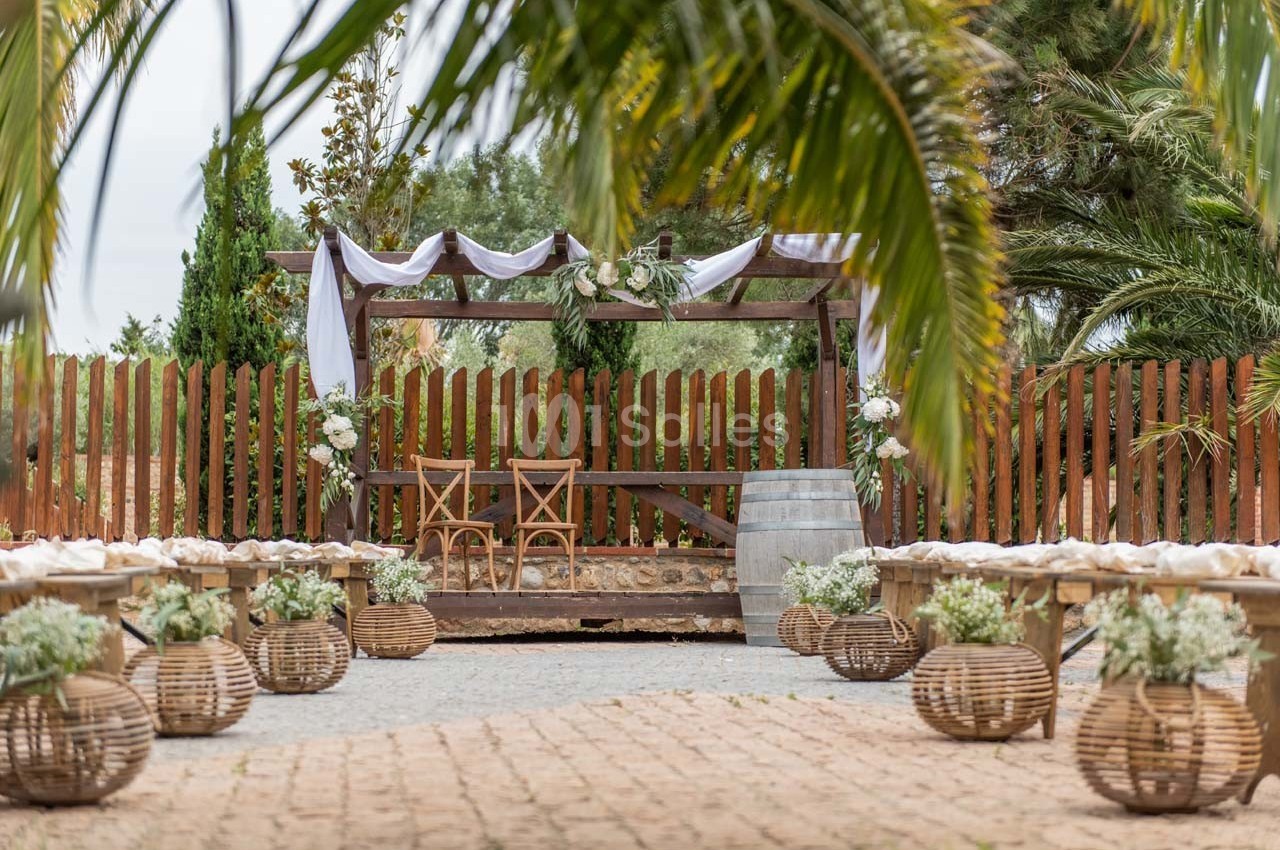 Espace extérieur décoré pour une cérémonie, avec arche en bois, chaises, paniers fleuris et allée pavée.
