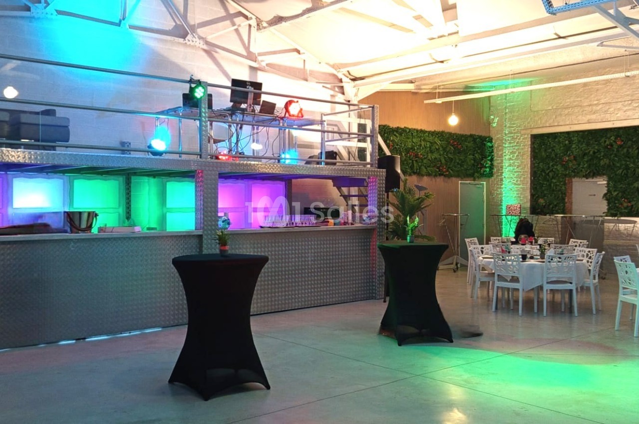 Salle moderne avec mezzanine, éclairages colorés, tables dressées et plantes décoratives.