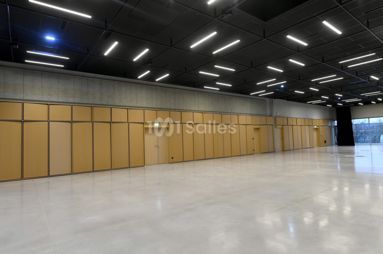 Salle vide avec sol en béton poli, murs en panneaux de bois clair et plafond noir avec éclairage LED rectangulaire.