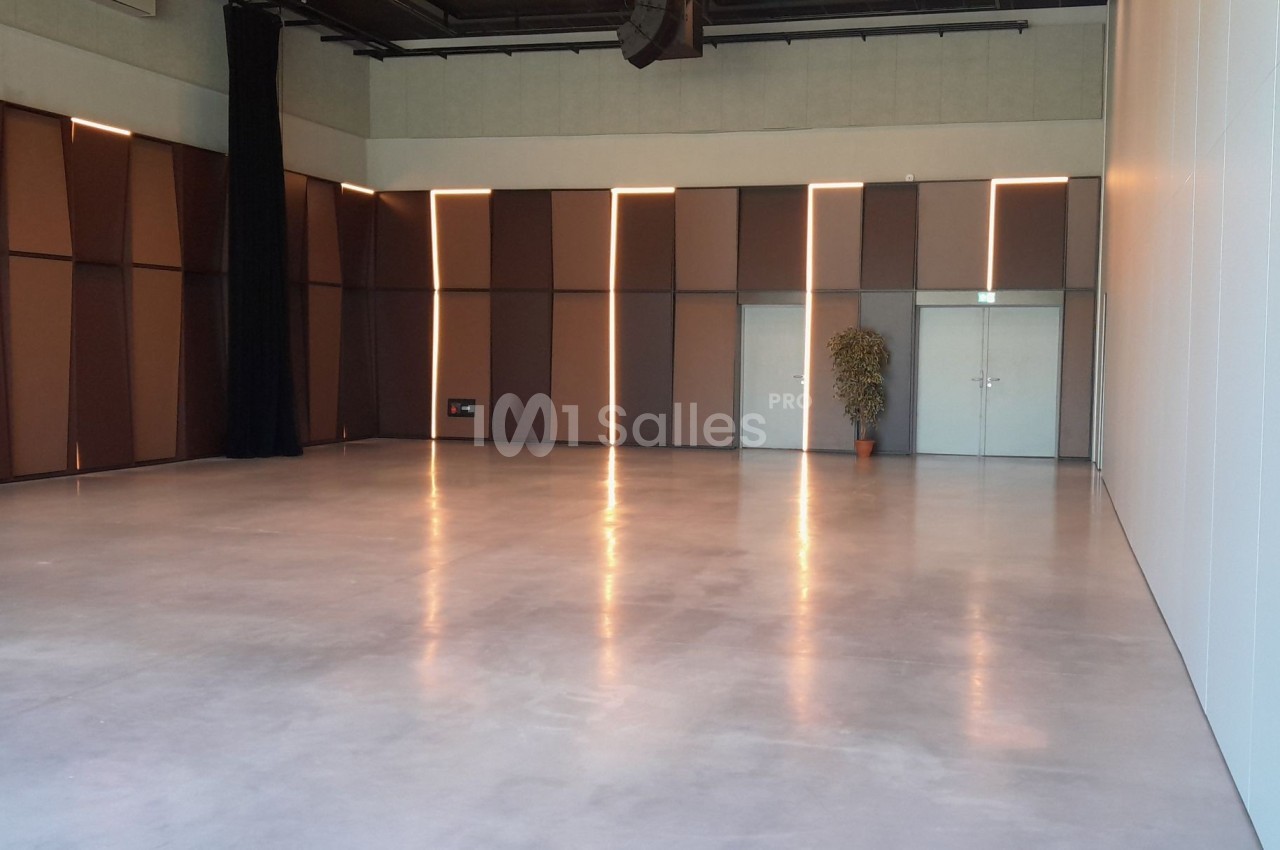 Salle vide avec sol en béton poli, murs bruns et blancs, éclairage doux et une plante près des portes blanches.