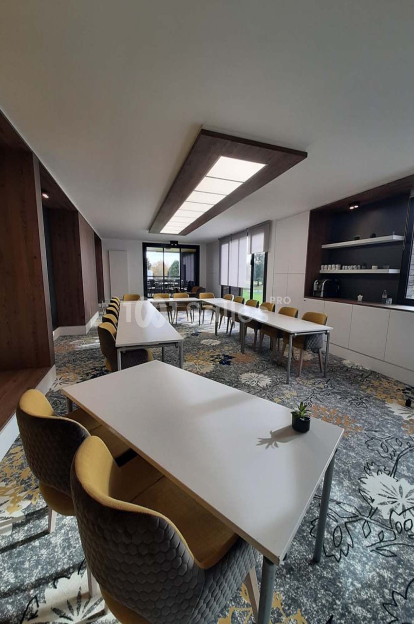 Salle de réunion lumineuse avec tables blanches, chaises jaunes et grises, et étagères avec vaisselle en arrière-plan.