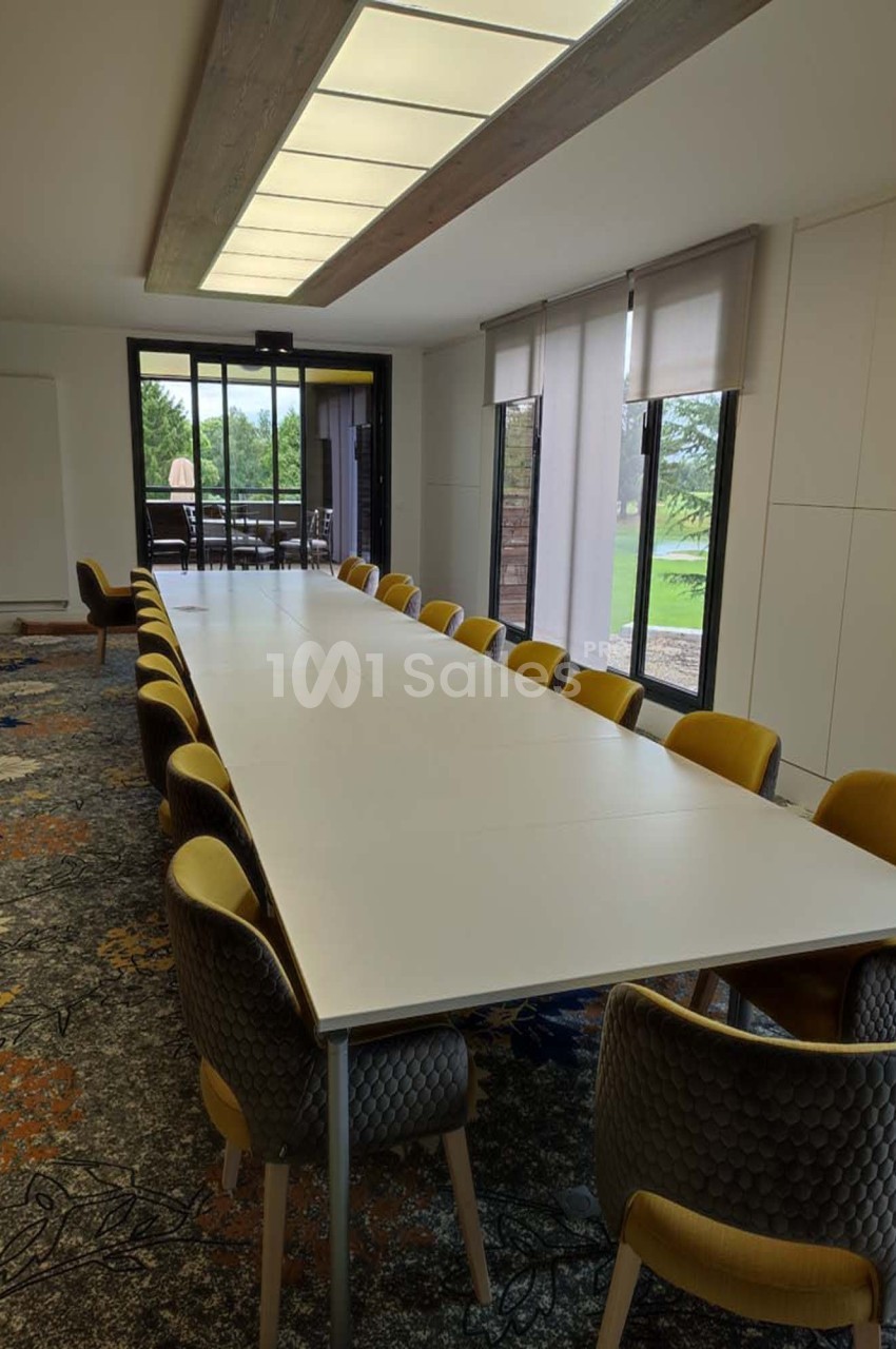 Salle de réunion lumineuse avec une grande table blanche entourée de chaises jaunes et grises, vue sur un espace extérieur…