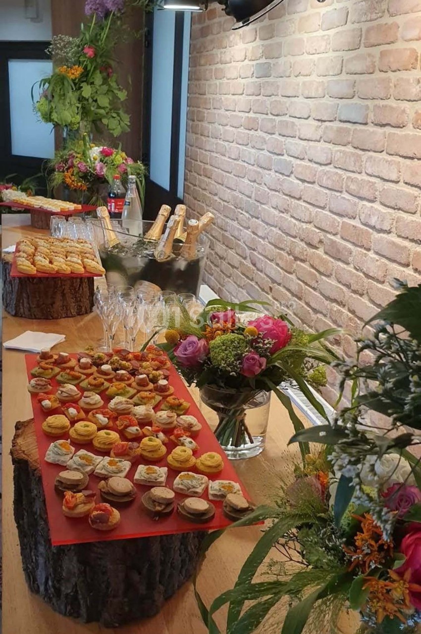 Plateau de bouchées apéritives variées disposé sur une table en bois, décorée de fleurs et de bouteilles.
