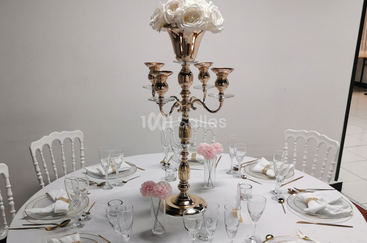 Table élégamment dressée avec un chandelier doré, des roses blanches et roses, et une vaisselle raffinée.