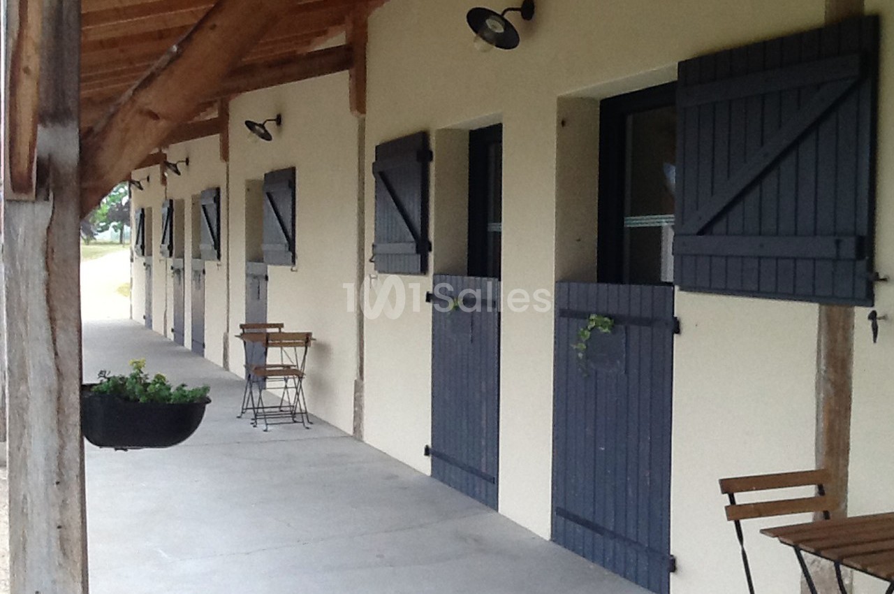 Façade d'un bâtiment avec des volets bleus, des tables en bois et un toit en bois sous une galerie couverte.