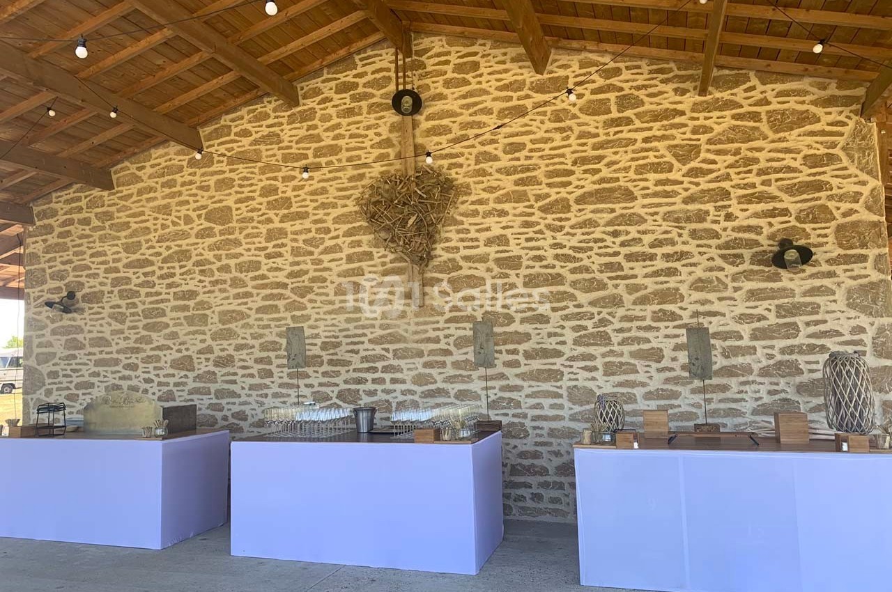 Tables de buffet alignées sous un auvent en bois, devant un mur en pierre avec des décorations murales.
