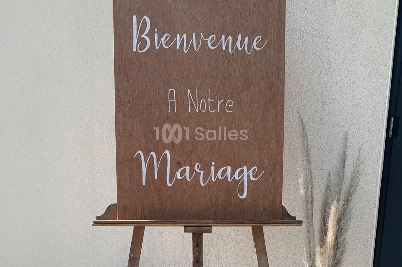 Panneau en bois sur un chevalet avec l'inscription ’Bienvenue à notre mariage’, décoré de pampas à droite.