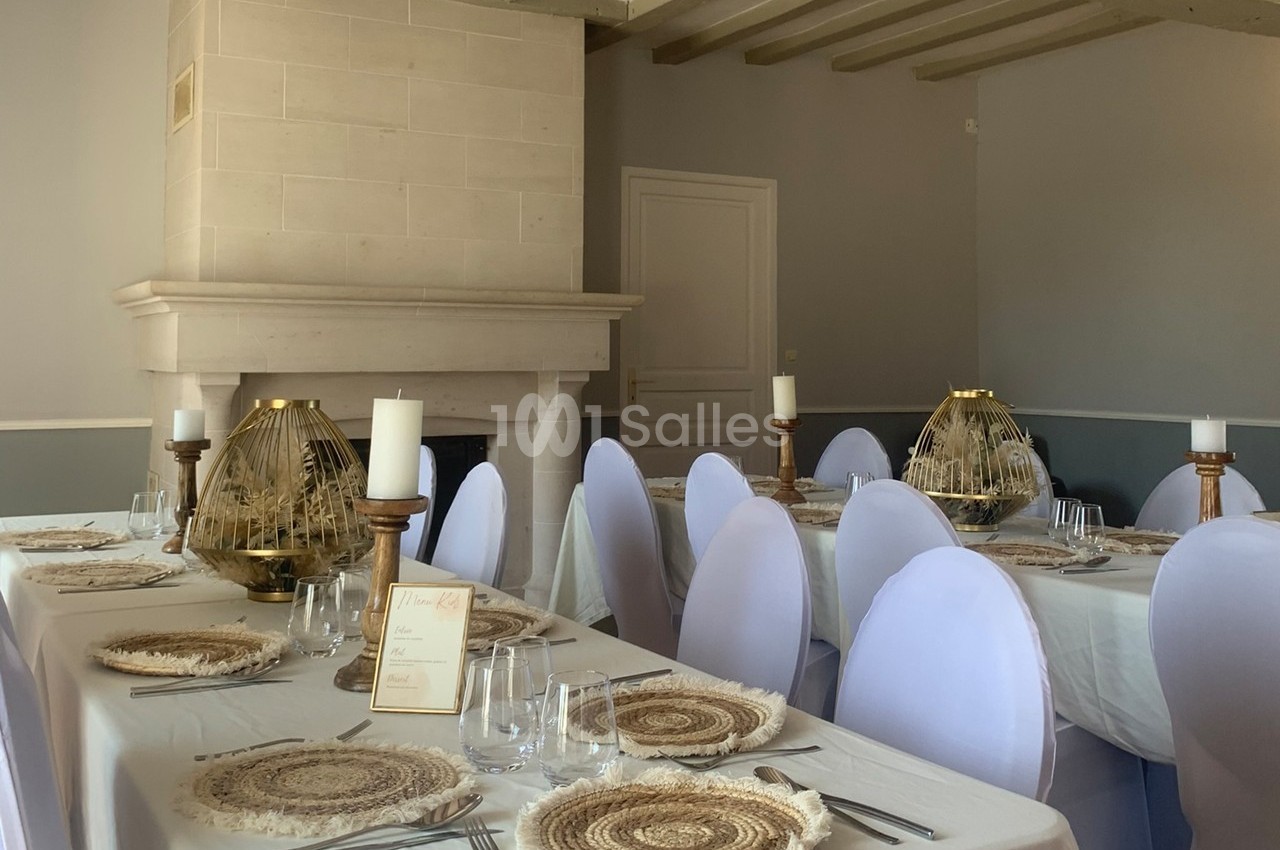 Salle de réception avec tables dressées, nappes blanches, assiettes en fibres naturelles et bougeoirs décoratifs.