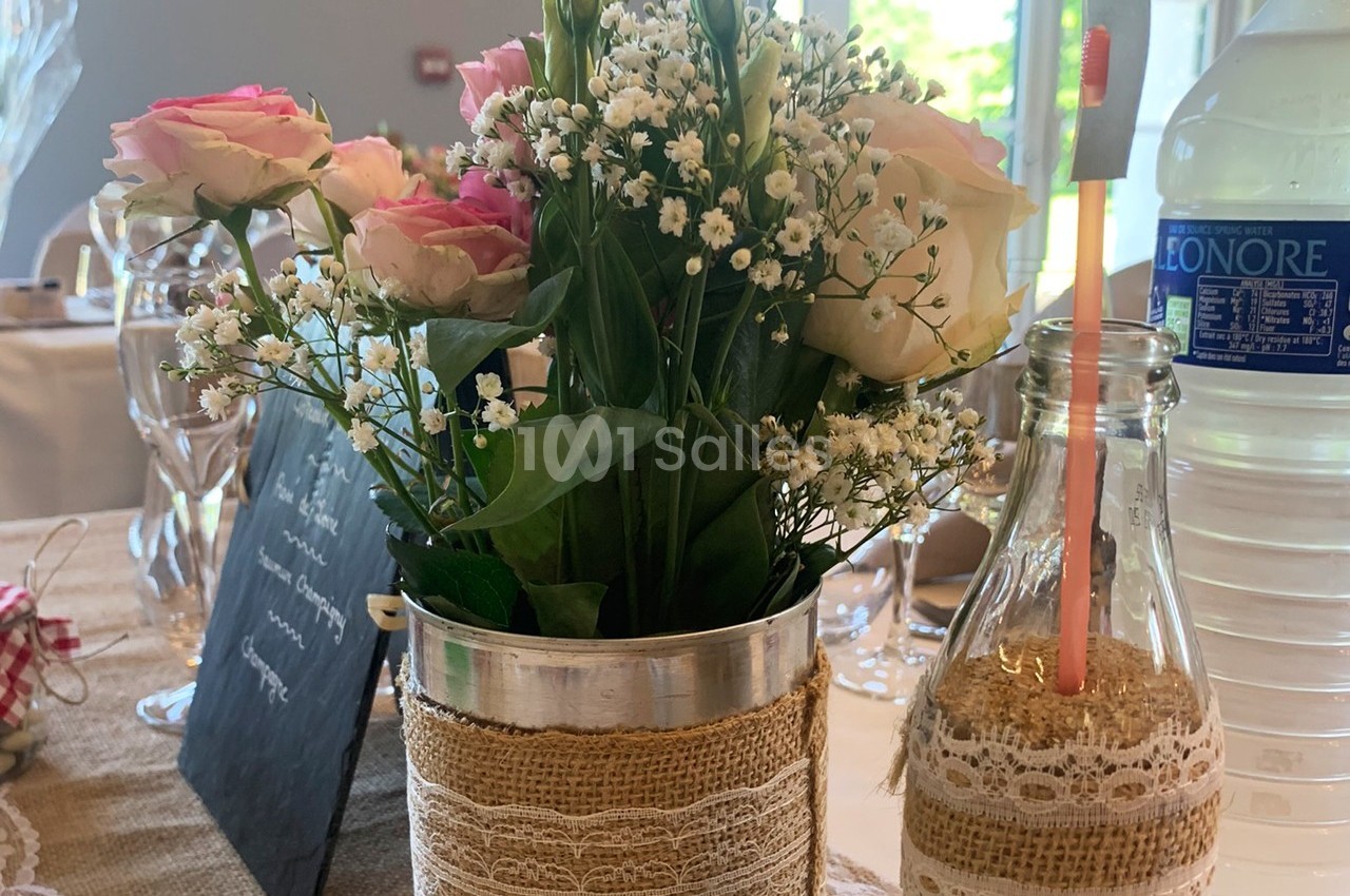 Arrangement floral avec roses et gypsophiles dans un pot décoré de toile de jute, posé sur une table de réception.