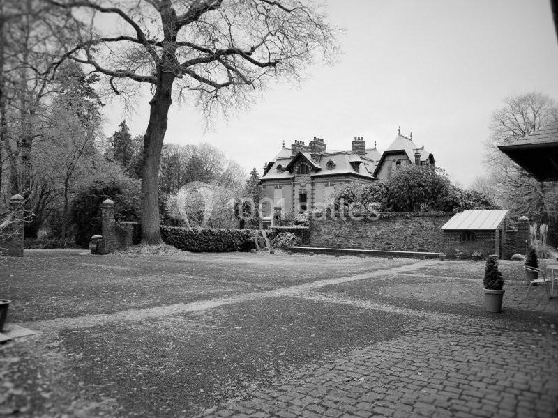 Cour pavée avec un grand arbre, un manoir ancien en arrière-plan et des murs en pierre entourant le site.