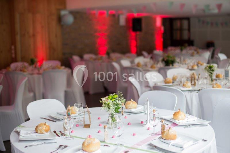 Salle de réception décorée avec des tables rondes, nappes blanches, vaisselle élégante et éclairage rouge.