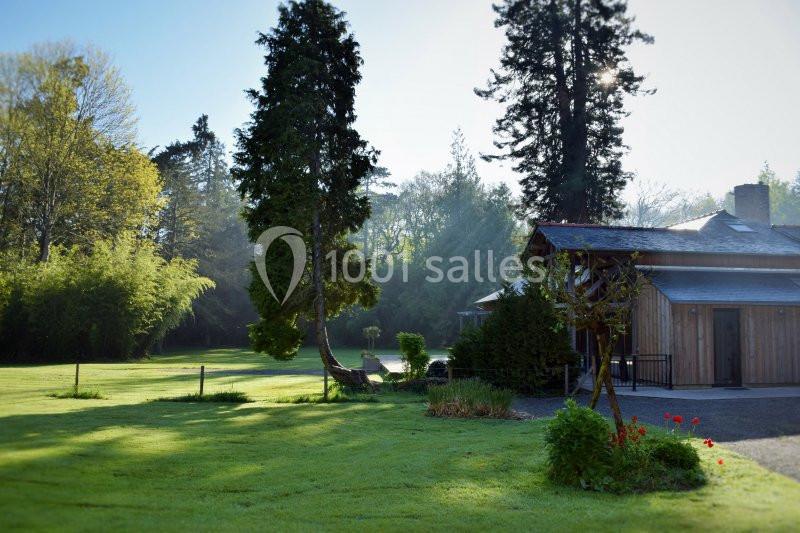 Jardin verdoyant avec pelouse, arbres et une maison en bois éclairée par une lumière matinale.