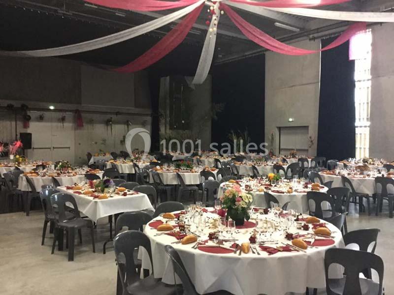 Salle de réception décorée avec des tables rondes dressées pour un événement, ornées de nappes blanches et de fleurs.
