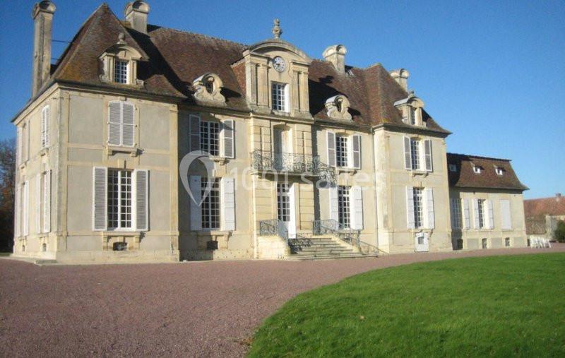 Façade d'un château ancien en pierre avec toit en tuiles, volets blancs et pelouse au premier plan.