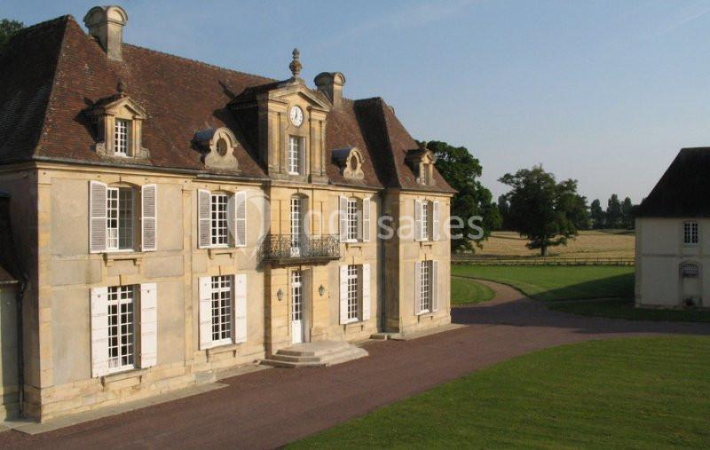 Façade d'un manoir en pierre avec toit en ardoise, entouré de pelouses et d'un chemin gravillonné.
