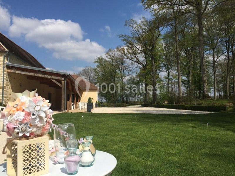 Extérieur d'une maison en pierre avec terrasse, pelouse verte, arbres en arrière-plan et décorations de mariage au premier…
