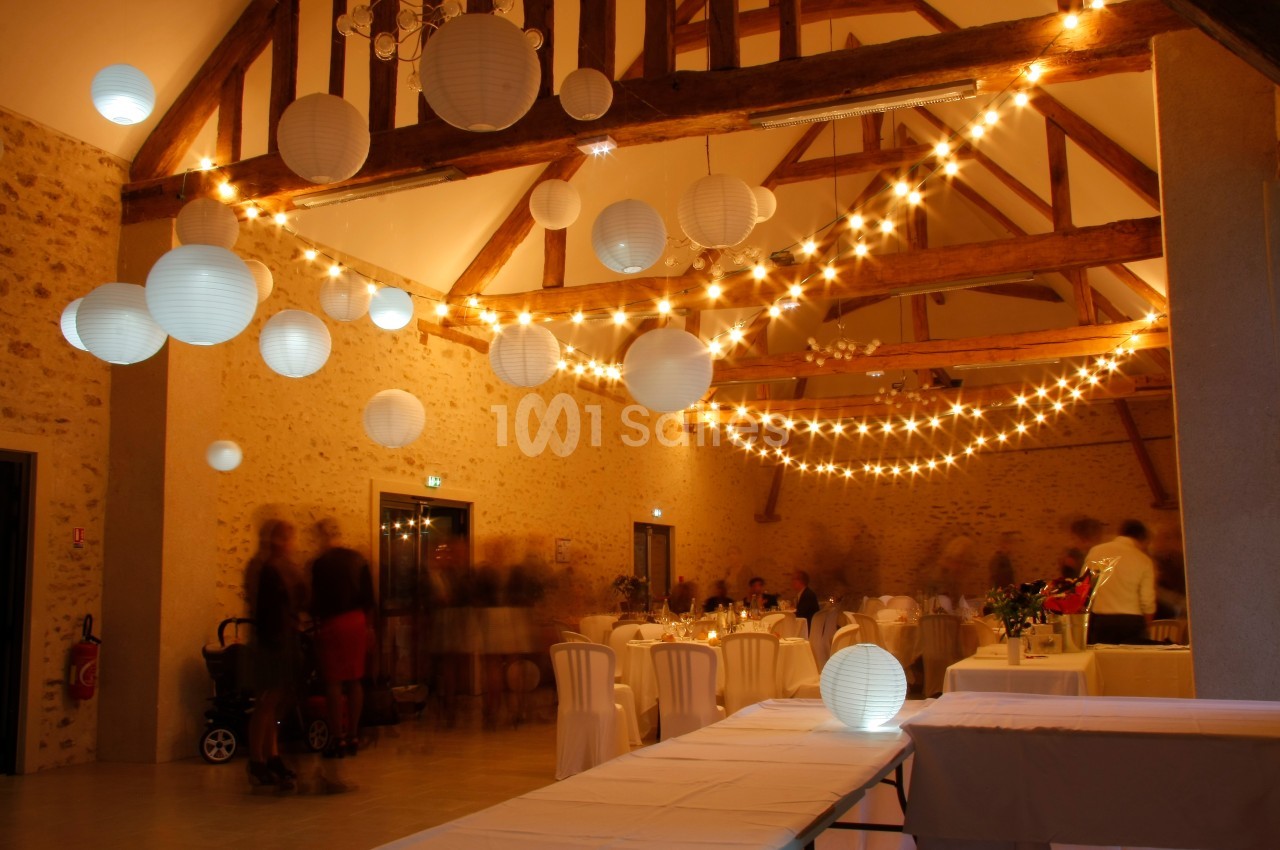 Salle de réception avec poutres apparentes, décorée de guirlandes lumineuses et lanternes suspendues.