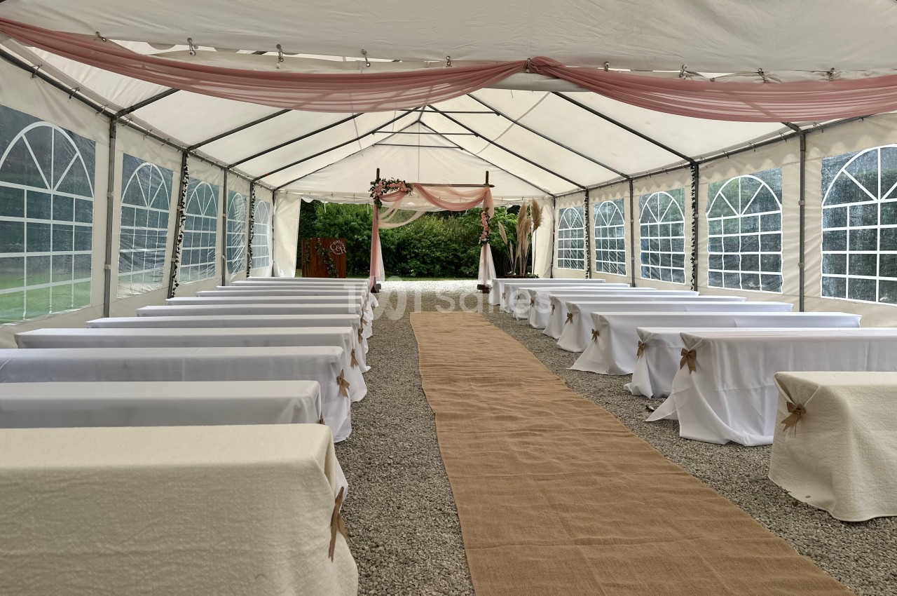 Intérieur d'une tente de réception avec allée centrale en toile, bancs et décoration pour une cérémonie en plein air.