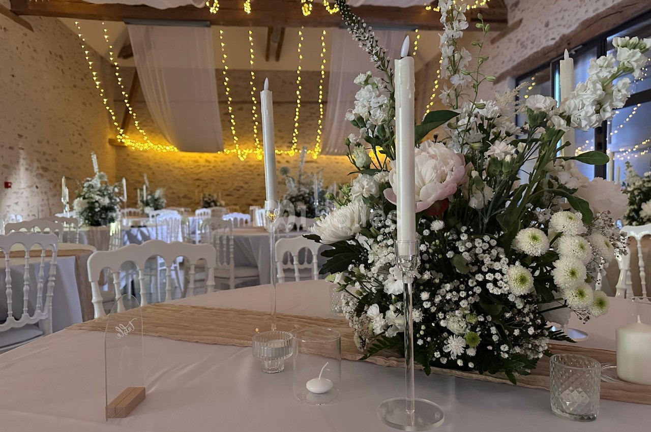 Salle de réception décorée avec des guirlandes lumineuses, des fleurs blanches et des bougies sur des tables dressées.
