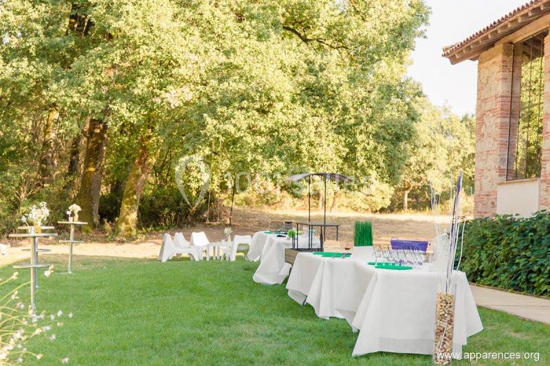 Tables dressées pour un événement en extérieur, installées sur une pelouse près d'arbres et d'un bâtiment en briques.