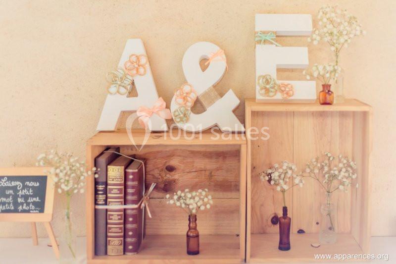 Lettres décoratives ’A & E’ ornées de rubans et fleurs, entourées de livres, vases et gypsophiles sur des caisses en bois.