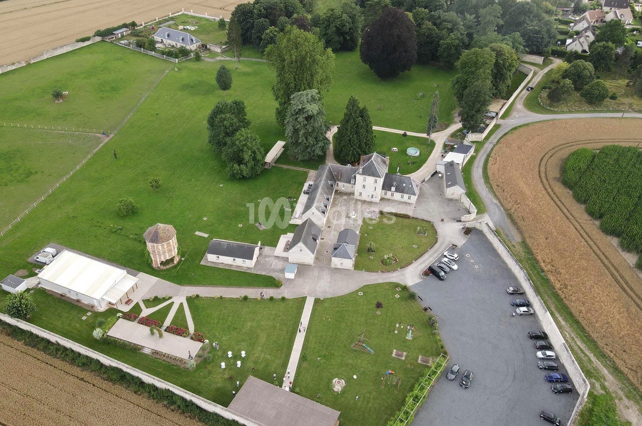 Vue aérienne d'un domaine avec bâtiments, espaces verts, parking et champs environnants.