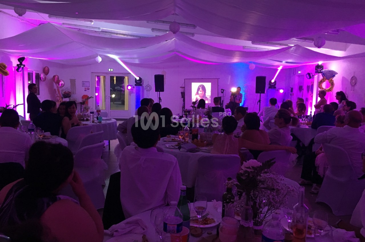 Salle de réception décorée avec des invités assis, éclairage coloré et projection d'une image sur un écran.