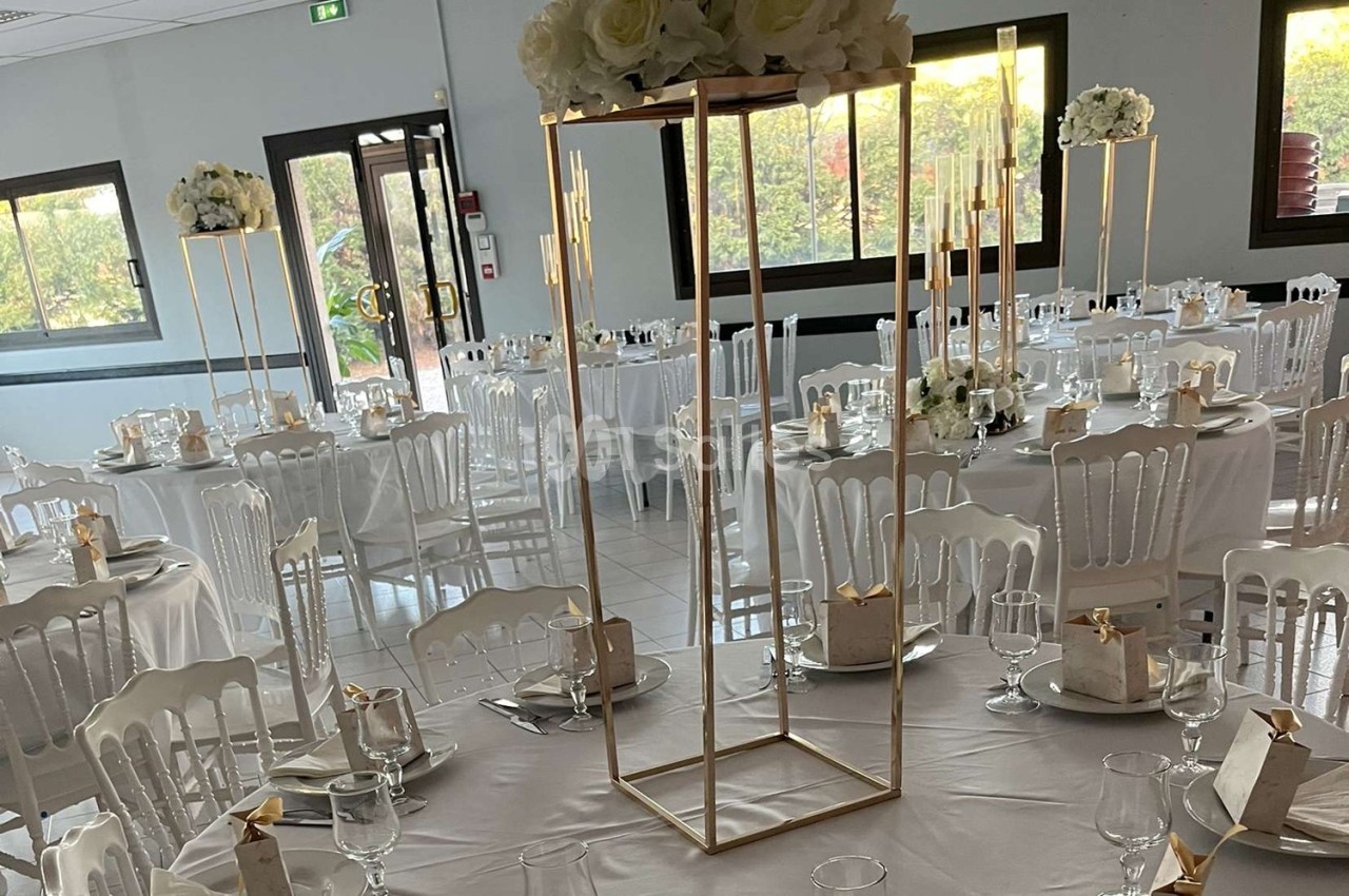 Salle de réception décorée avec des tables rondes, nappes blanches, chaises assorties et centres de table floraux.