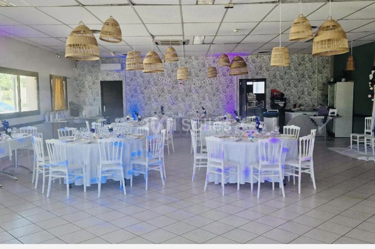 Salle de réception décorée avec des tables rondes dressées, des chaises blanches et des suspensions en osier.