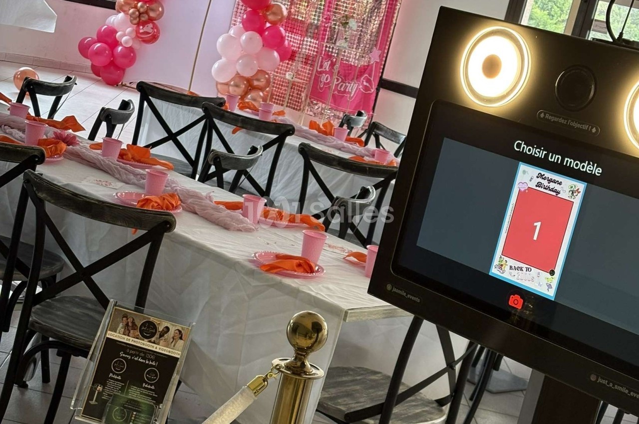 Salle décorée pour un événement avec une table dressée et une borne photo interactive au premier plan.