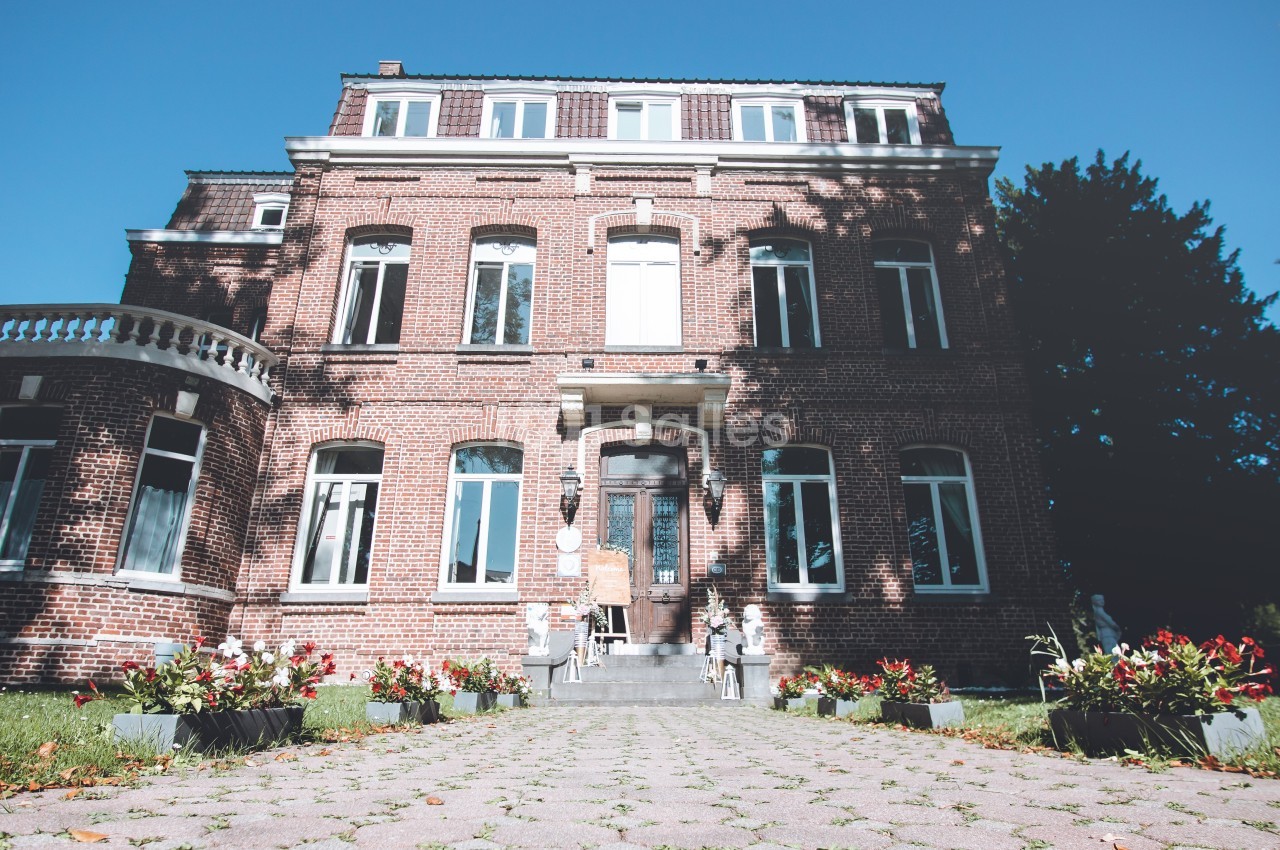 Façade d'une grande maison en briques rouges avec allée pavée et parterres de fleurs au premier plan.