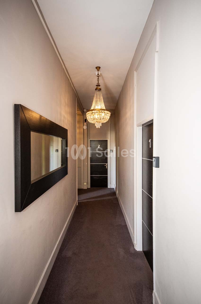 Couloir étroit avec moquette, miroir mural, lustre suspendu et portes numérotées 1 et 2 au fond.