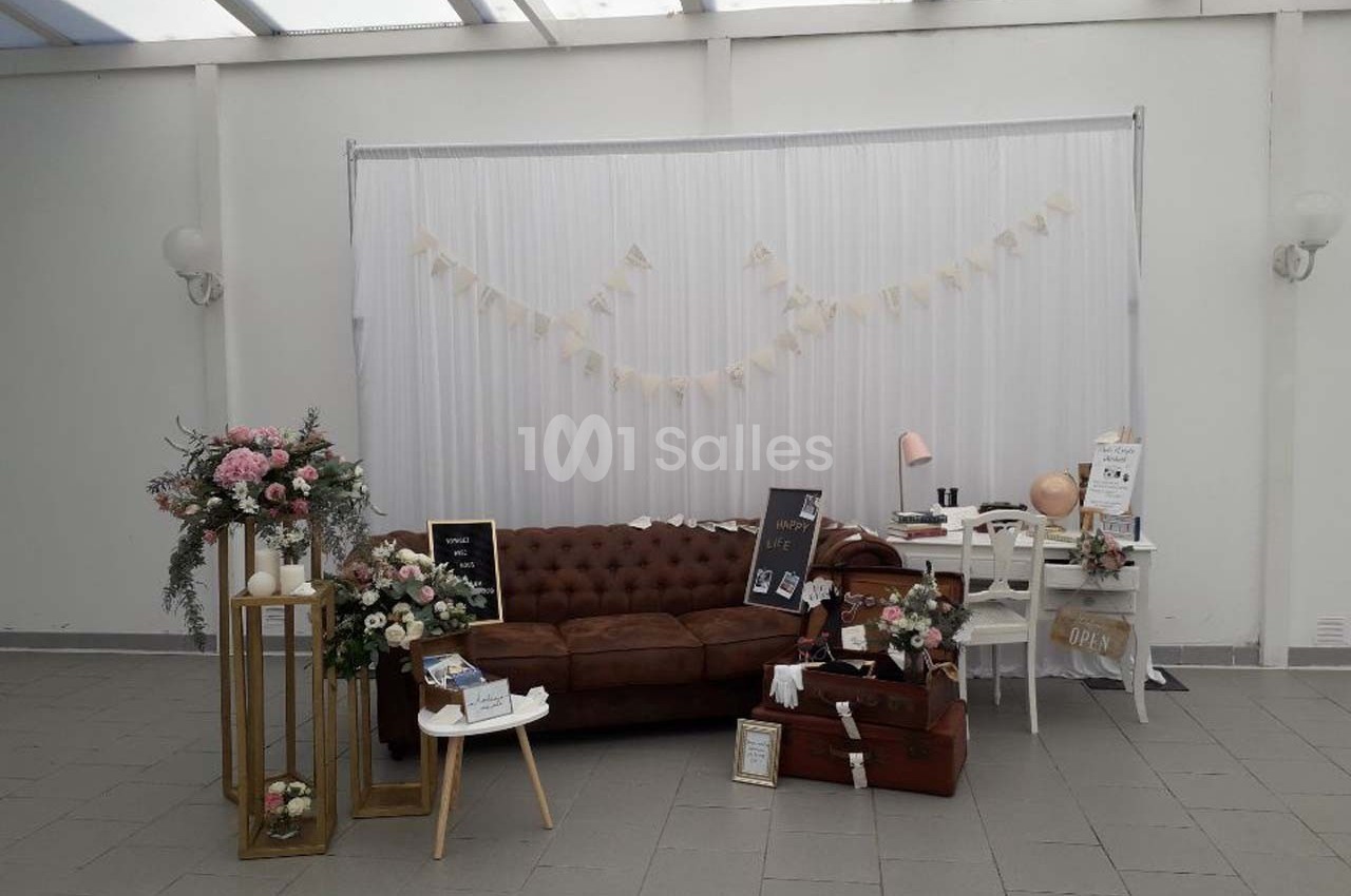 Décoration intérieure avec canapé en cuir, fleurs, valises et guirlandes dans un espace lumineux à fond blanc.