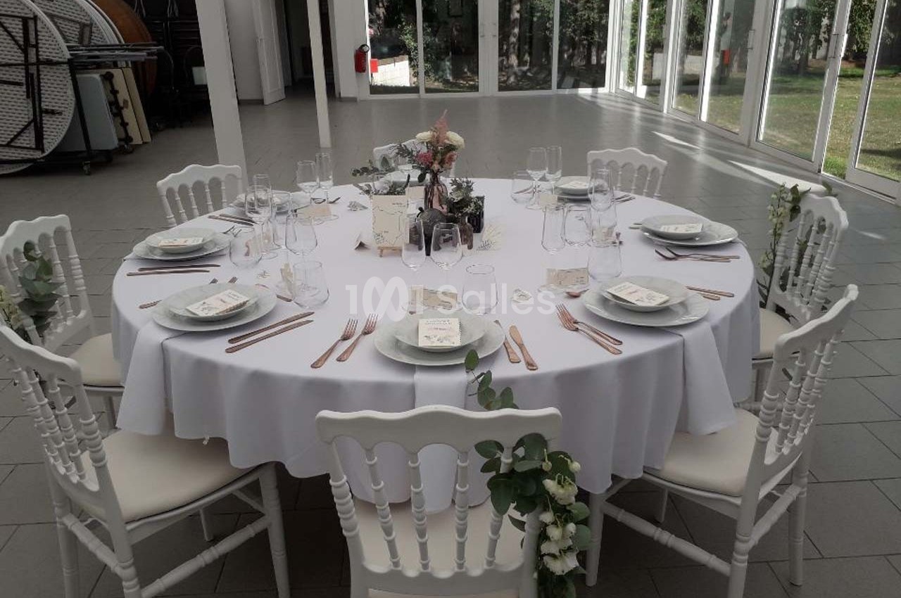 Table ronde dressée pour un événement, avec nappes blanches, vaisselle élégante et décoration florale.