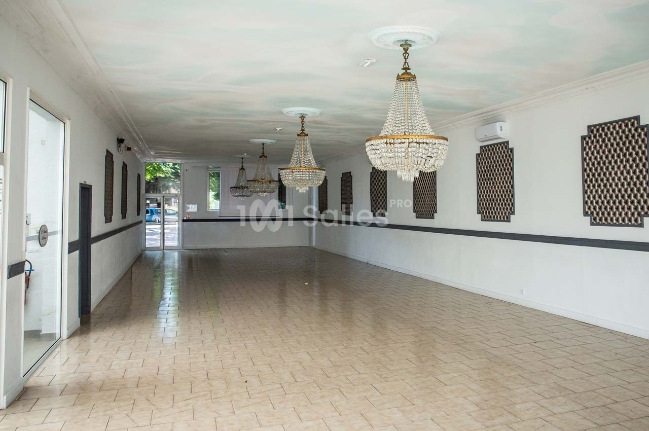 Salle vide avec sol carrelé, murs blancs ornés de panneaux décoratifs et lustres suspendus au plafond.