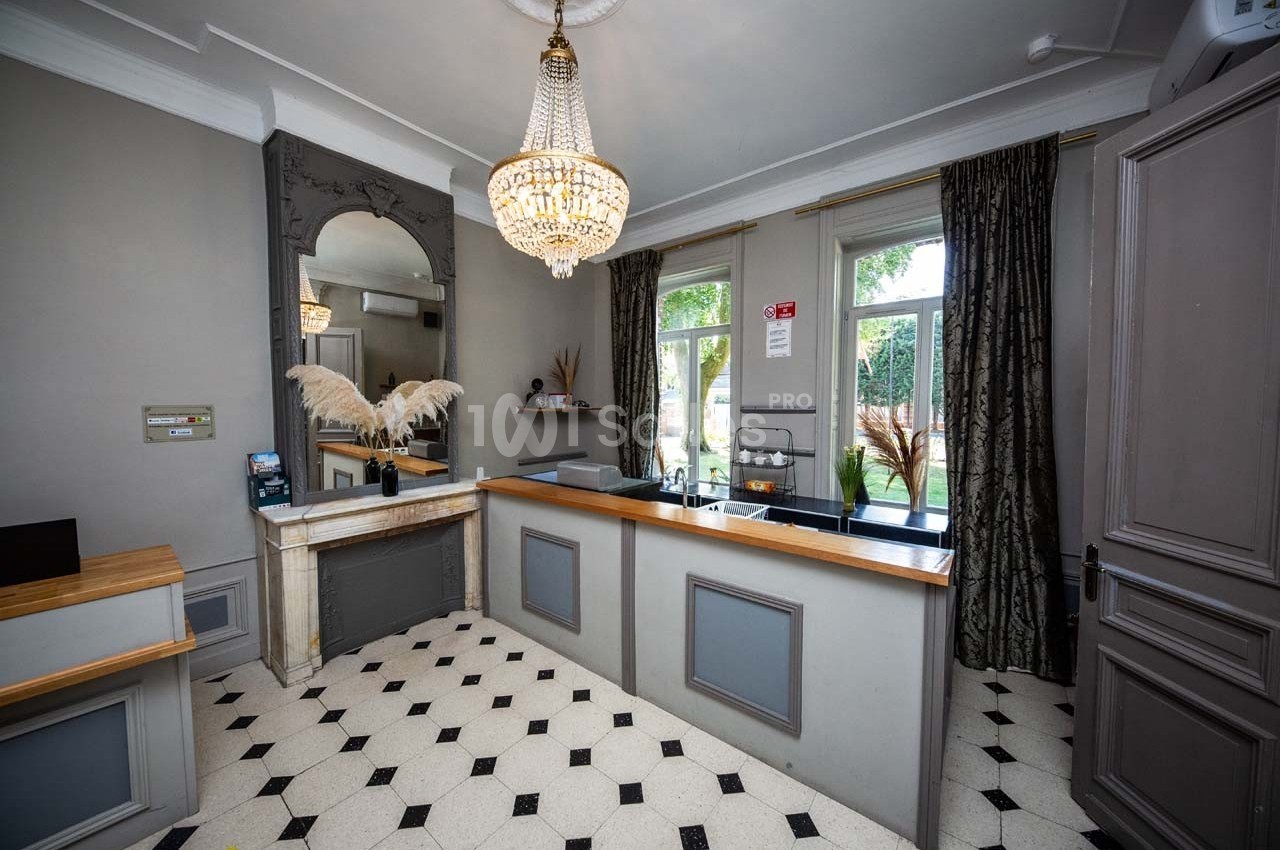 Réception d'un hôtel avec comptoir en bois, lustre élégant, miroir orné et sol carrelé noir et blanc.