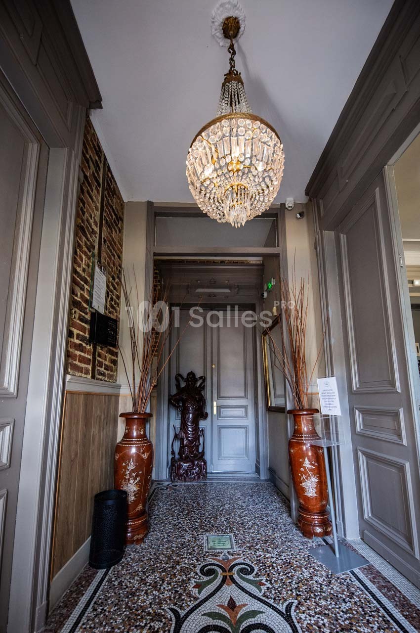 Entrée élégante avec un sol en mosaïque, un lustre en cristal, deux vases décoratifs et une statue en bois.