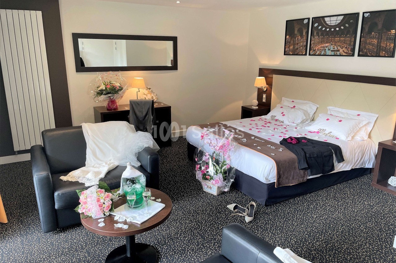 Chambre d'hôtel décorée pour une occasion spéciale, avec lit parsemé de pétales et bouquets de fleurs.