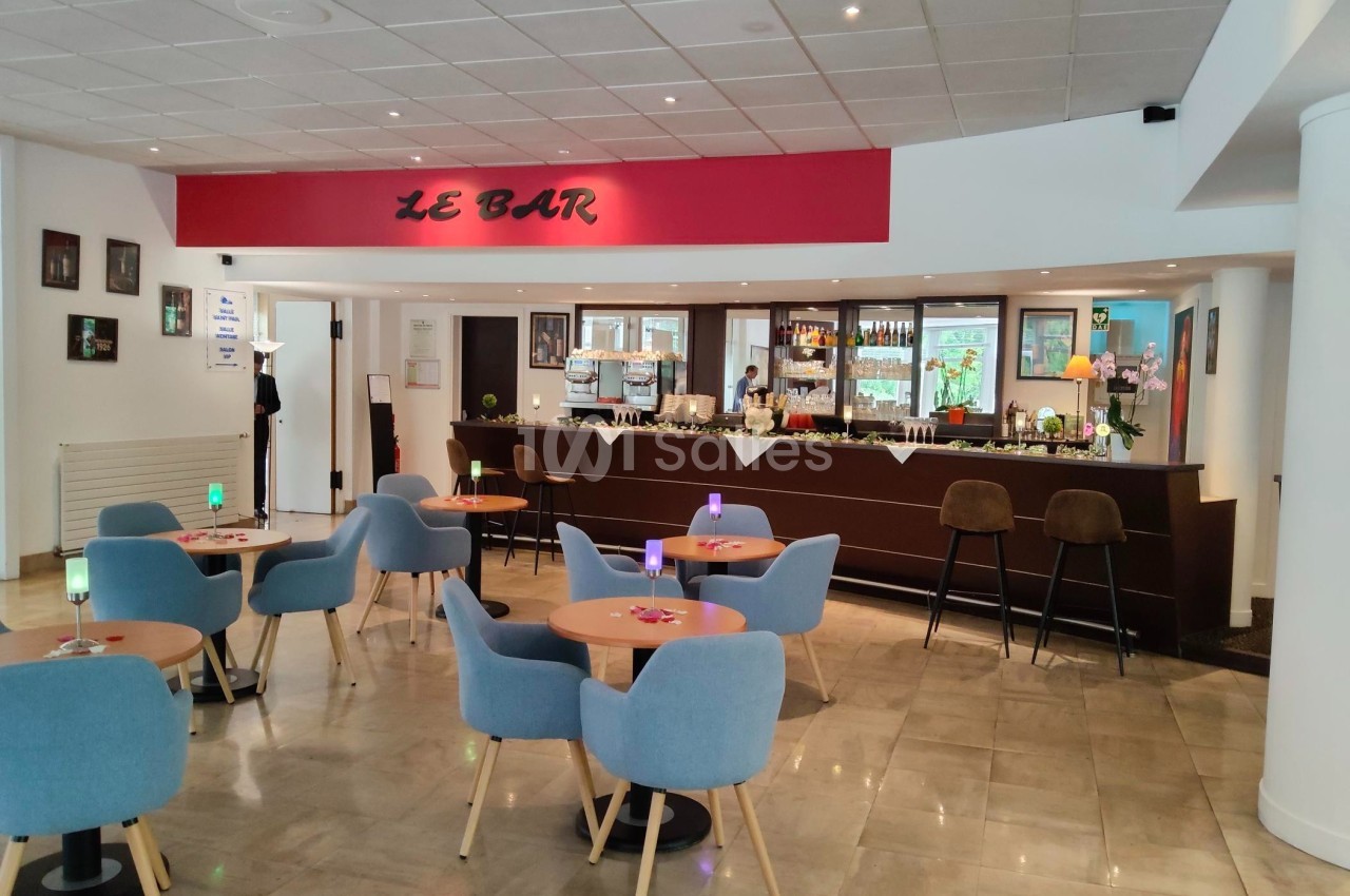 Salle de bar moderne avec tables, chaises bleues, comptoir en bois sombre et décoration murale.