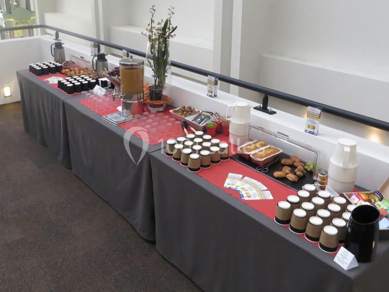 Buffet avec boissons chaudes, jus, viennoiseries et fruits disposés sur une table recouverte d'une nappe grise.
