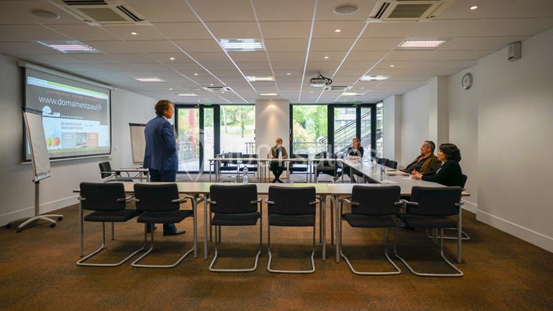Un homme en costume donne une présentation devant un petit groupe de personnes dans une salle de réunion lumineuse.
