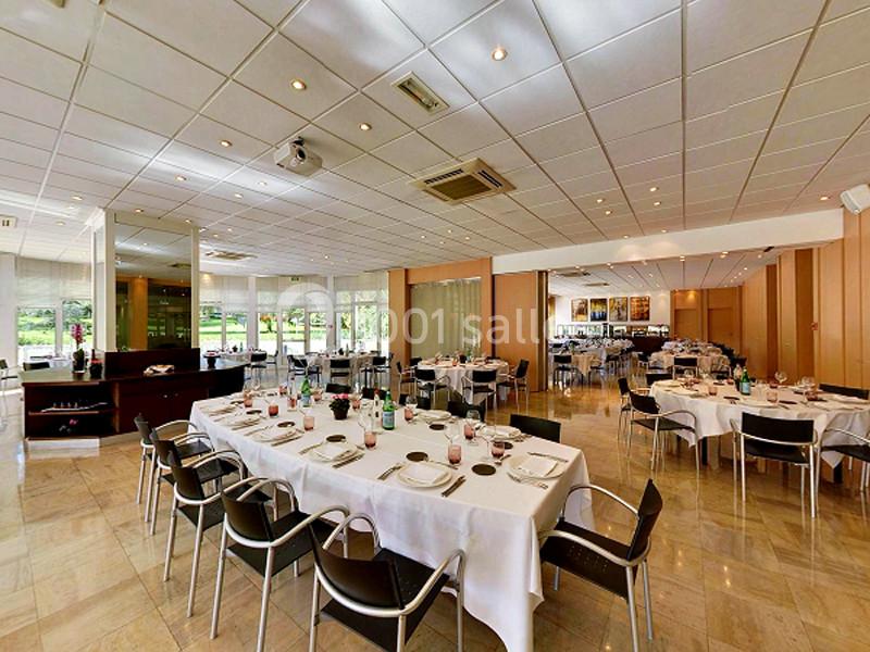 Salle de restaurant lumineuse avec tables dressées, chaises noires et grandes baies vitrées donnant sur un espace vert.