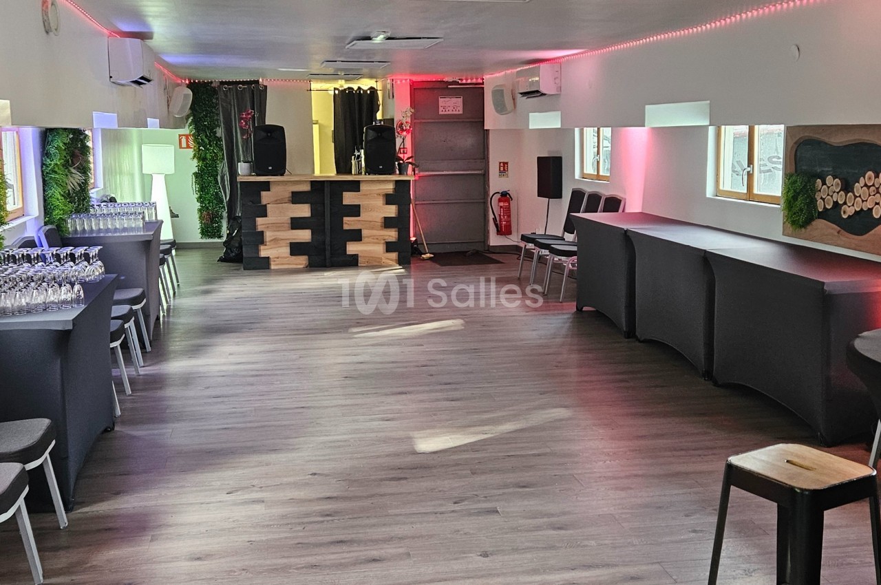 Salle lumineuse aménagée avec des tables hautes, chaises, décorations murales et un comptoir au fond.