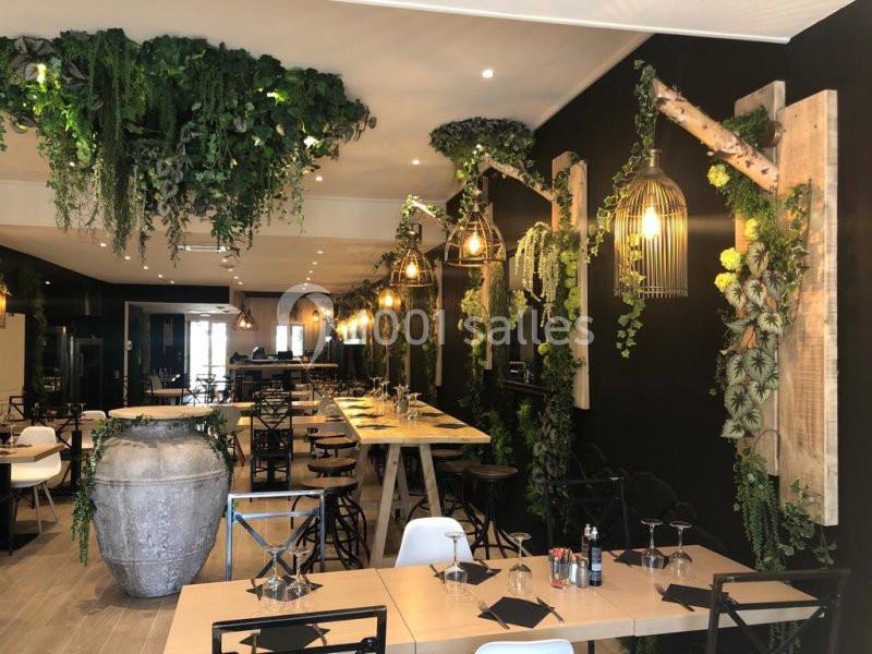 Salle de restaurant décorée de plantes suspendues et murales, avec des tables en bois et des chaises modernes.